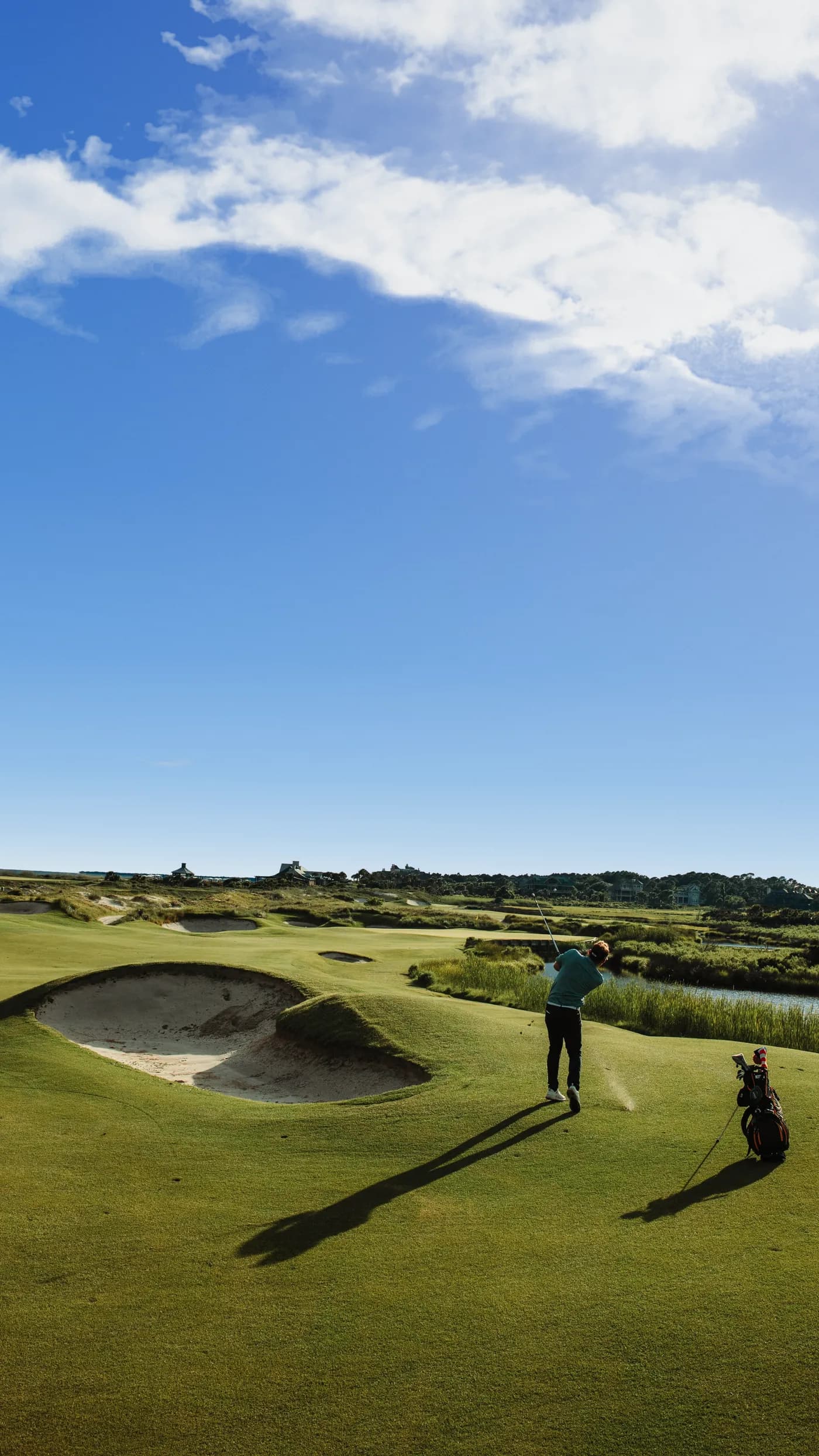 Golfare slår ut på en linksbana med bunker under blå himmel